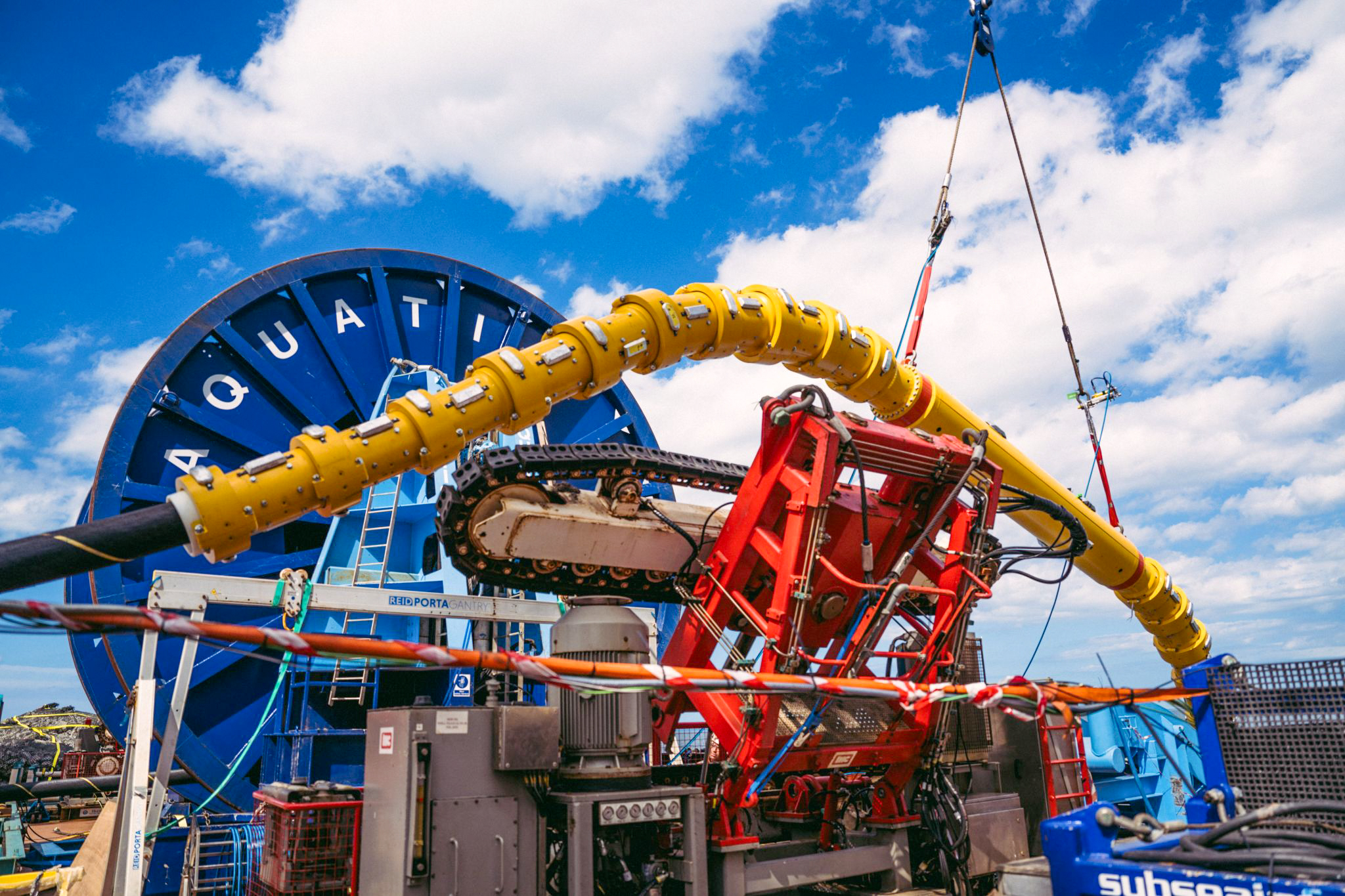 Red and white cable tensioner in breakback mode as a yellow cable protection system passes through. Blue sky background