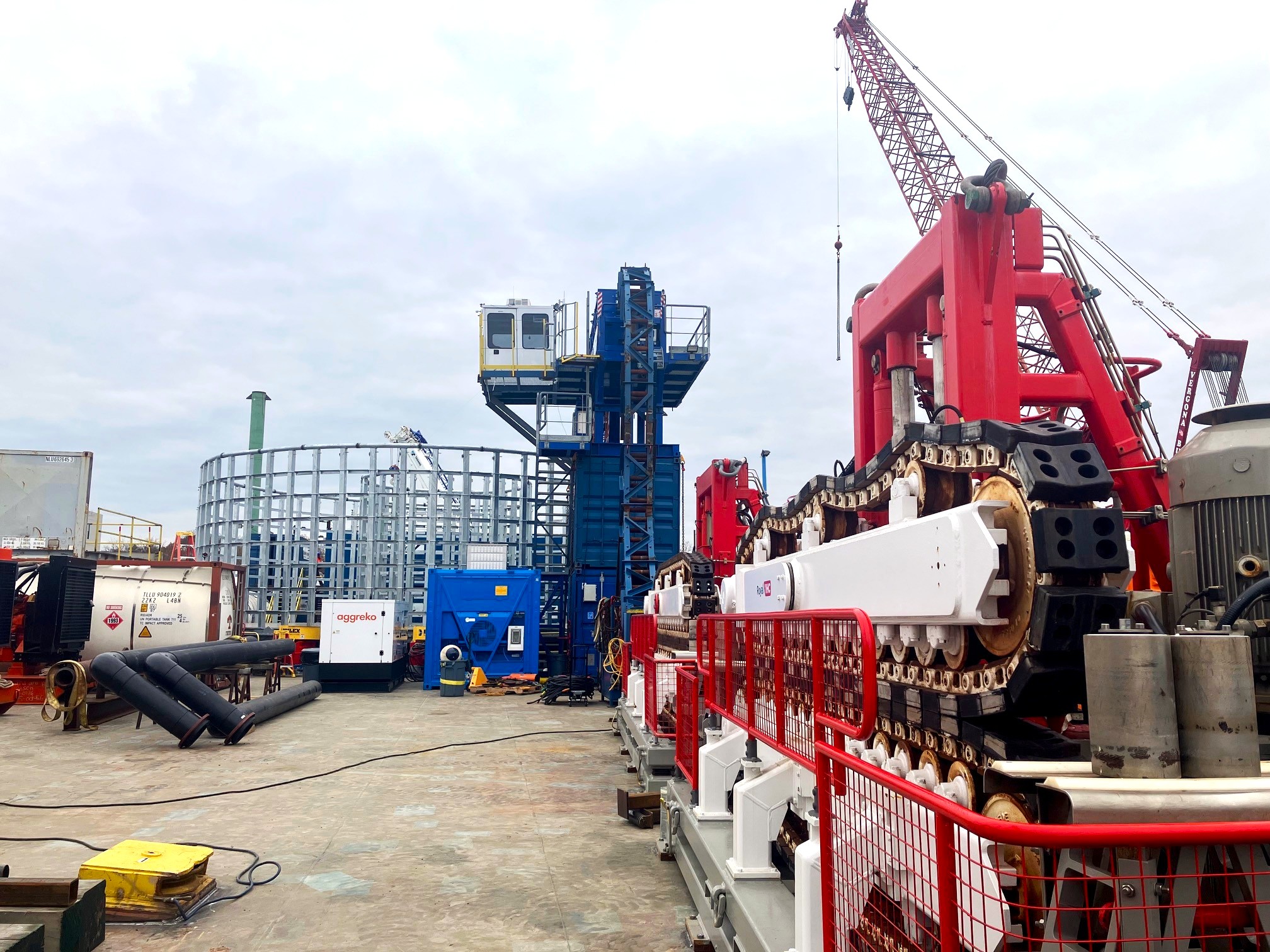 Two red and white cable tensioners lined up on the back of a vessel, with a blue cable carousel in the background. Grey cloudy skies behind.