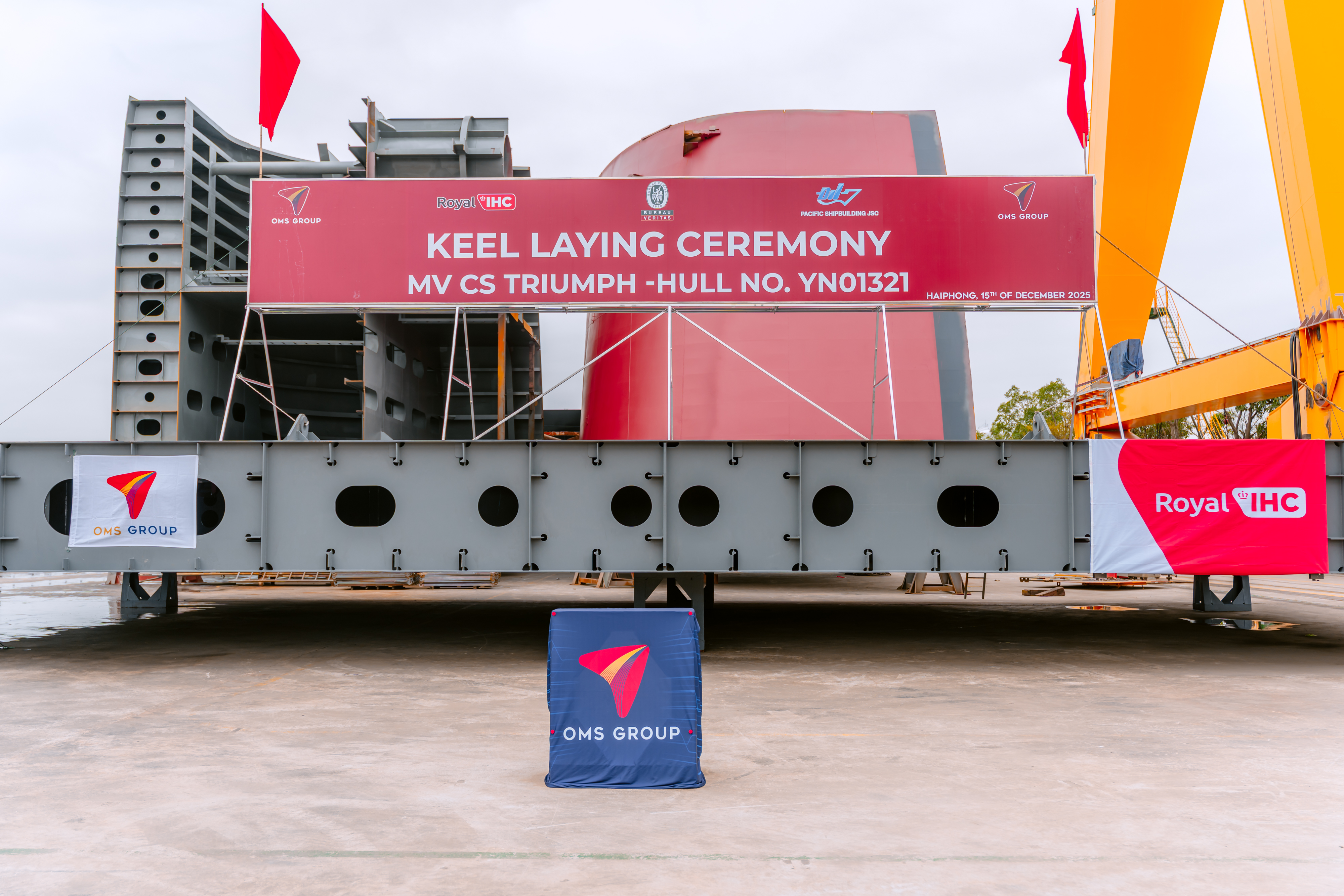 Keel for CS Triumph at a shipyard, featuring a large sign and company banners from Royal IHC and OMS Group.