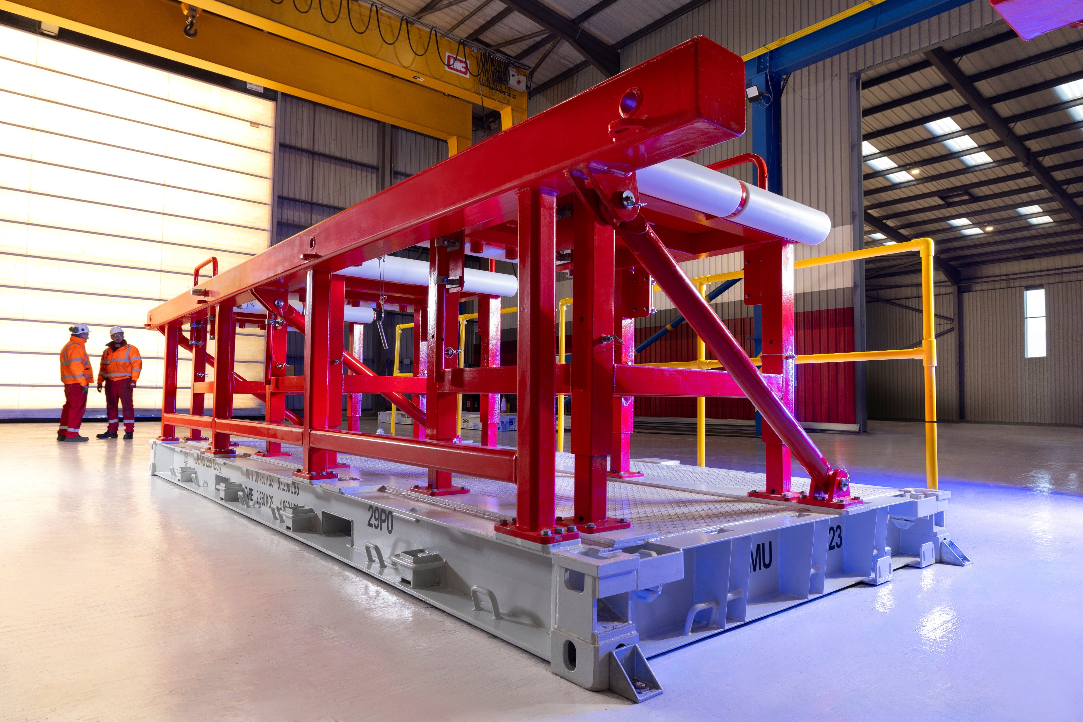 Set in a large factory bay, a set of red framed roller tables on a grey built-in pallet.
