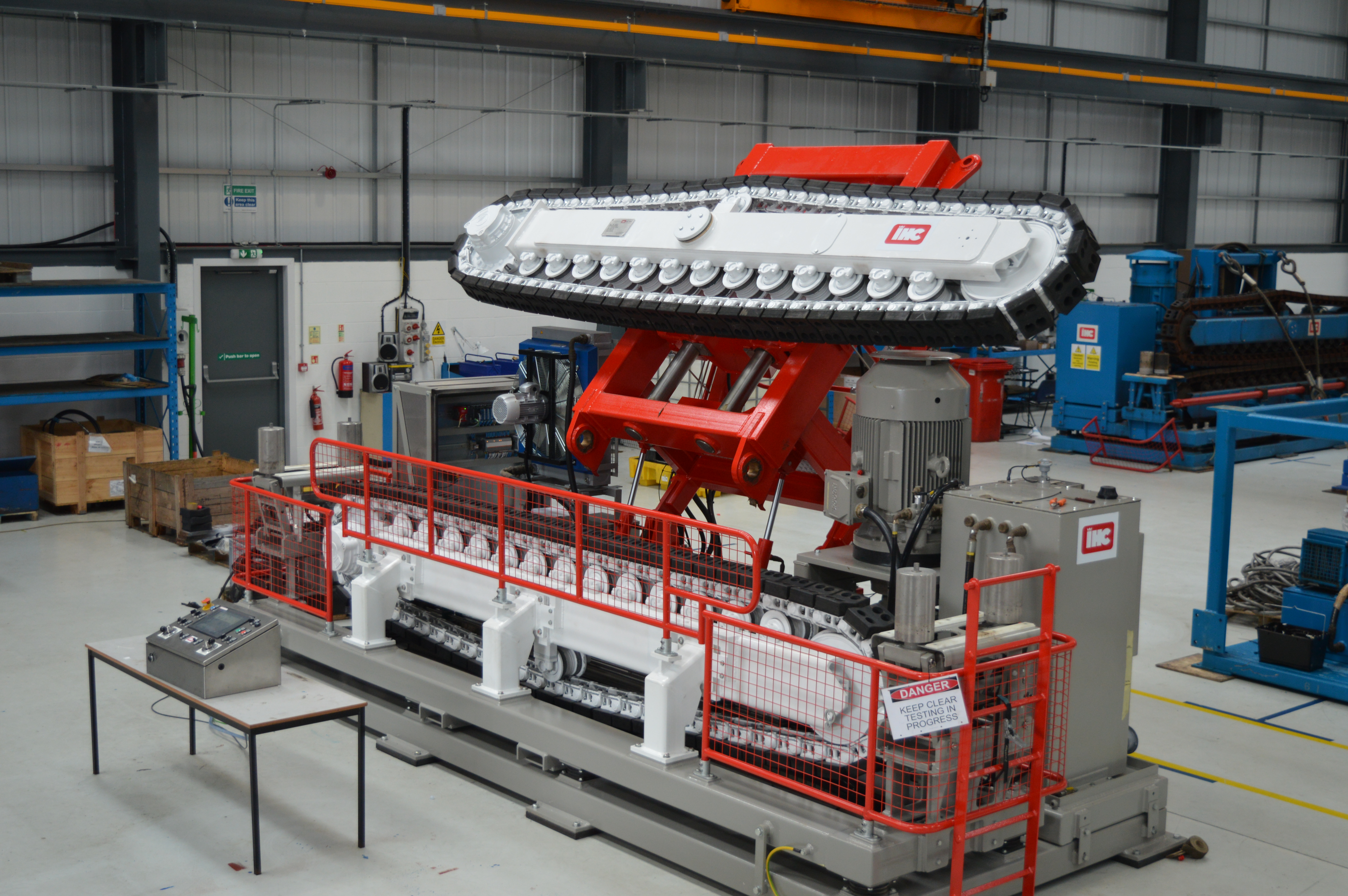 Red and white two-track cable tensioner demonstrating full breakback functionality in a factory setting.