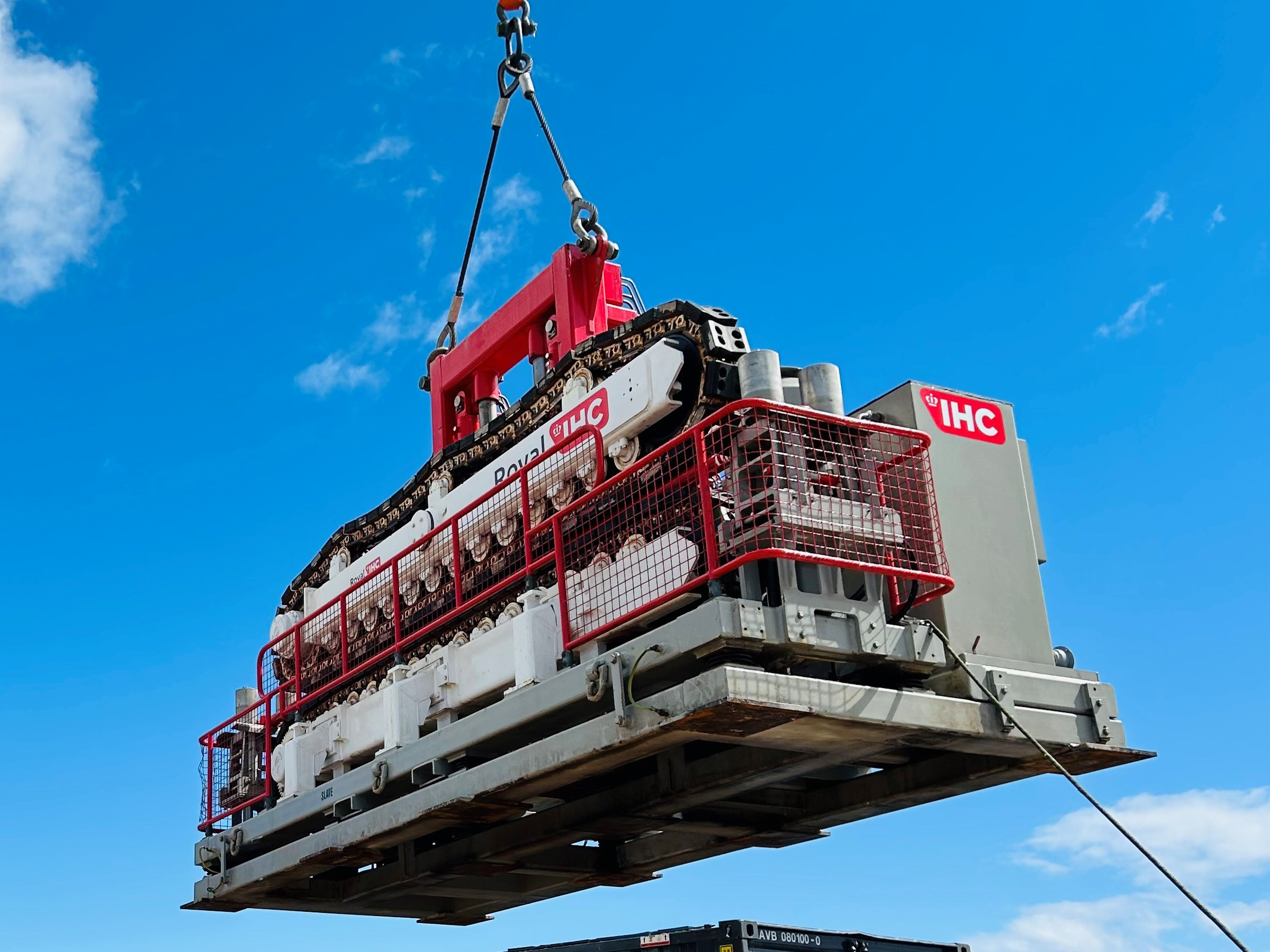 Red and white two-track cable tensioner being lifted against a blue sky background.
